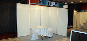 Stand esquina de 3x2m con cenefa impresa, cubre piso, iluminación, 1 mesa y 2 sillas.